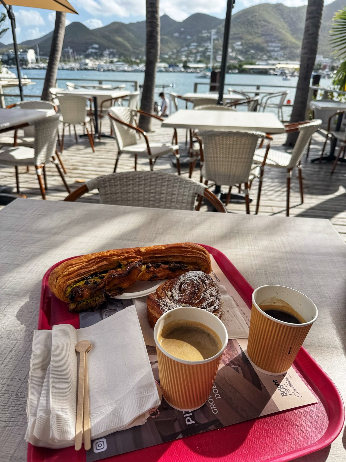 Breakfast tray with a pastry and two coffees on La Sucrière's lagoon-side terrace